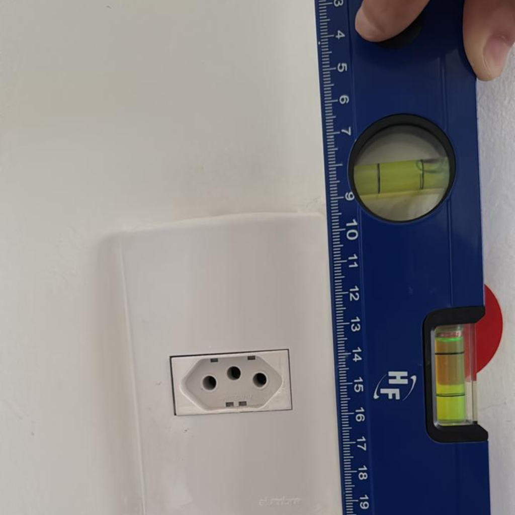 Inspeção de engenharia com nível de mão em vistoria de entrega, comprovando tomada fora do prumo e desalinhada no Rio de Janeiro.
